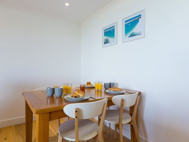 A dining table set with croissants juice and mugs in a room with white walls and wooden floor at Kernow's Dream in Carbis Bay