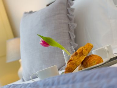 A bed with gray pillow a tray holding white cups a glass with a pink tulip and croissants at Kernow's Dream in Carbis Bay
