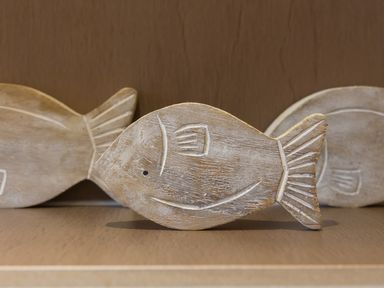 Three wooden fish-shaped decorative items placed on a wooden surface at Kernow's Dream in Carbis Bay