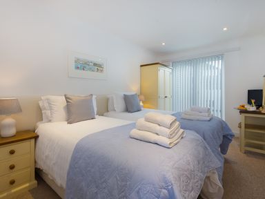 A bedroom with two single beds with folded towels bedside tables lamps wardrobe and a desk with a television at Kernow's Dream in Carbis Bay