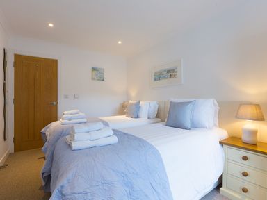 A bedroom with two single beds with folded towels bedside lamps and a wooden door at Kernow's Dream in Carbis Bay