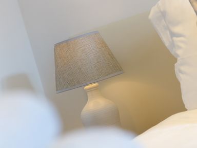 A beige table lamp next to a bed with white bedding in a bedroom at Kernows Dream in Carbis Bay
