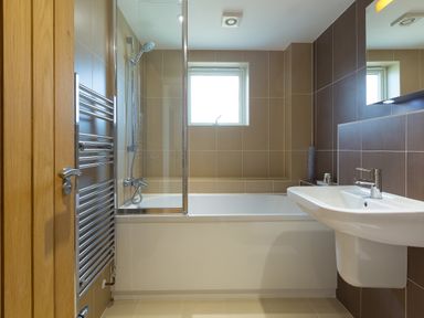 A bathroom with a bathtub shower combination a white sink and a window at Kernow's Dream in Carbis Bay