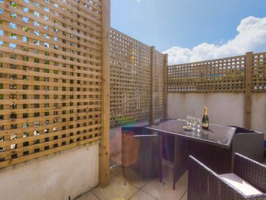 An outdoor patio with wicker chairs and a glass table with a bottle and glasses at Kernow's Dream in Carbis Bay