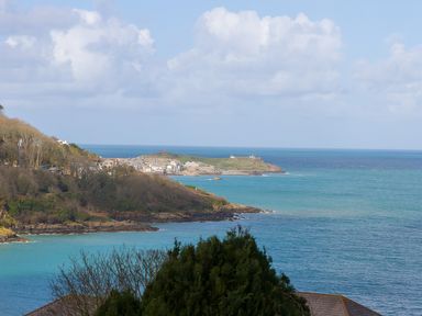 Coastal view of a bay with blue water cliffs vegetation and distant buildings at Kernow's Dream in Carbis Bay