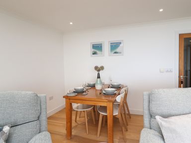 A dining table set with plates bowls glasses and a vase with flowers in a room with two grey chairs at Kernow's Dream in Carbis Bay
