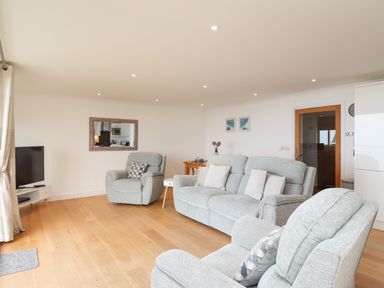 A living room with gray upholstered armchairs and sofa a TV on a stand and a wooden floor at Kernow's Dream in Carbis Bay