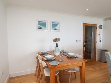 A dining area with a wooden table set for four with plates glasses and a vase with flowers at Kernow's Dream in Carbis Bay
