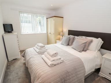 A bedroom with a bed towels on it a wardrobe a chest of drawers and a window at Kernow's Dream in Carbis Bay