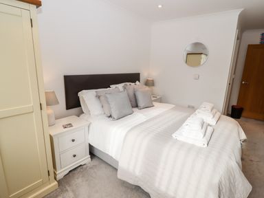 A bedroom with a double bed, pillows, bedside tables with lamps, a wardrobe, and towels on the bed at Kernow's Dream in Carbis Bay