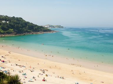 A beach with people on sand and in water near a green hillside at Ocean Cove in Carbis Bay