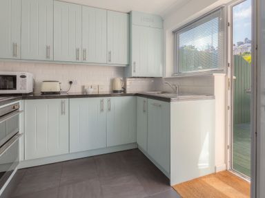 A kitchen with light blue cabinets a microwave toaster kettle sink and a door leading outside at Ocean Cove in Carbis Bay