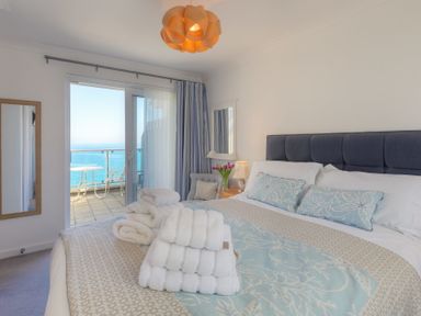 A bedroom with a bed and folded towels on it a lamp and flowers on a bedside table and a balcony with a table and chairs at Ocean Cove in Carbis Bay