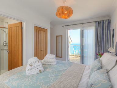 A bedroom with a bed folded towels balcony door and sea view at Ocean Cove in Carbis Bay