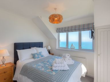A bedroom with a bed towels on it wooden bedside tables a window with an ocean view at Ocean Cove in Carbis Bay
