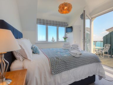 A bedroom with a bed lamp bedside table windows flowers and an open door leading to a balcony at Ocean Cove in Carbis Bay