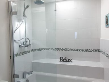A bathroom with a bathtub shower combination with glass partition and a relax sign on a tiled ledge at Ocean Cove in Carbis Bay