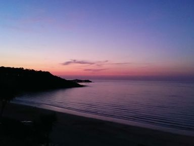 A beach with calm water and a hill in the background at sunset at Ocean Cove in Carbis Bay