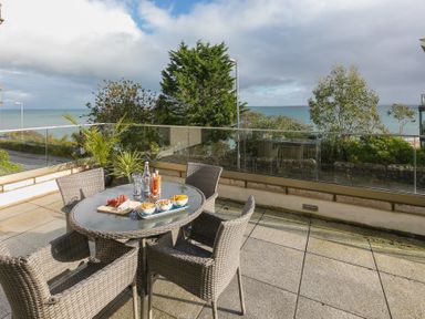 An outdoor patio with a round glass table and four wicker chairs overlooking the sea at The View in St Ives