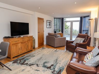 A living room with a wooden cabinet and television a gray armchair and brown leather sofas next to glass doors at The View in St Ives