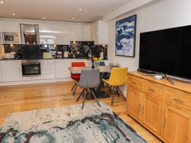 A modern kitchen and dining area with white cabinets and a large TV on a wooden stand at The View in St Ives