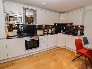 A kitchen with white cabinets black backsplash and wooden floor with red and blue chairs at The View in St Ives