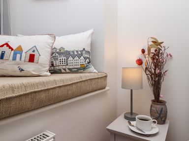 A window seat with decorative cushions next to a side table with a lamp a vase of dried flowers and a cup of coffee at The View in St Ives