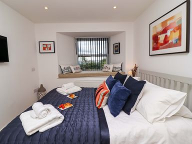 A bedroom with a bed with blue and white bedding and pillows towels on the bed and a window seat with cushions at The View in St Ives