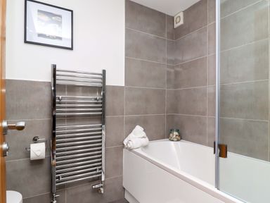 A bathroom with a bathtub towels towel rack and framed picture at The View in St Ives