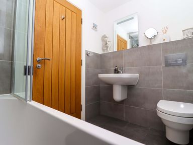 A bathroom with a wooden door a wall-mounted sink a toilet a bathtub with glass screen and a mirror above the sink at The View in St Ives