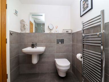 A bathroom with a wall-mounted sink and toilet a heated towel rail and decorative items at The View in St Ives
