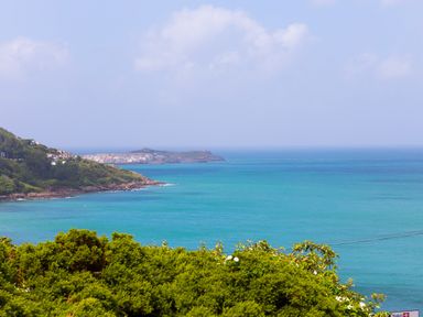 A coastal view with green shrubs in the foreground blue sea and a headland with buildings at Portside in Carbis Bay