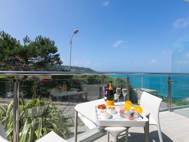 A balcony with a small table set with drinks and snacks overlooking the sea at Portside in Carbis Bay