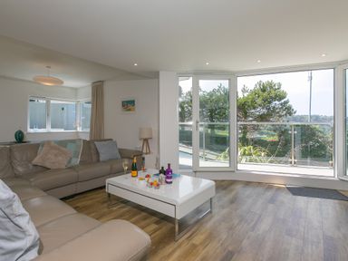 A living room with a beige sofa coffee table with drinks and snacks and glass doors overlooking greenery at Portside in Carbis Bay