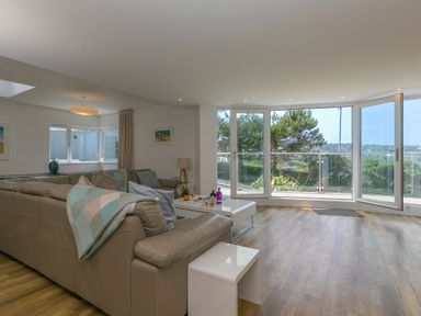 A living room with a sectional sofa a coffee table and open windows overlooking trees at Portside in Carbis Bay