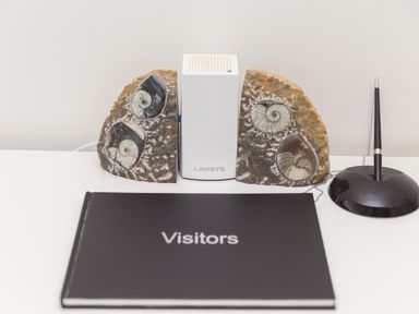 A visitor book on a desk with a Linksys device and ammonite fossil bookends with a black pen in a stand