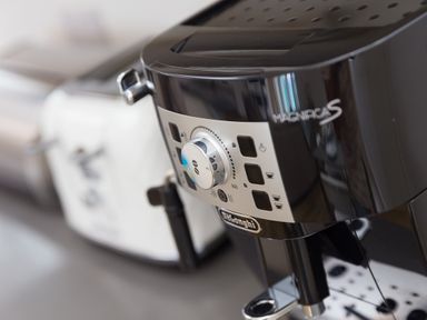 A black DeLonghi Magnifica S coffee machine on a kitchen counter with a white toaster in the background