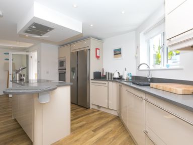 A kitchen with an island, stainless steel refrigerator, built-in microwave and oven, wooden floor, and a window at Portside in Carbis Bay