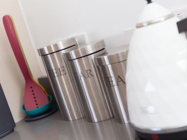 Three stainless steel canisters labeled coffee sugar and tea next to a white electric kettle and kitchen utensils in a container at Portside in Carbis Bay