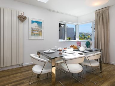 A dining area with a table set for breakfast and four white chairs near corner windows with a view at Portside Carbis Bay