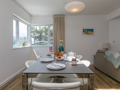 A dining table set for breakfast with plates cups and croissants in a room with windows and a sofa at Portside in Carbis Bay