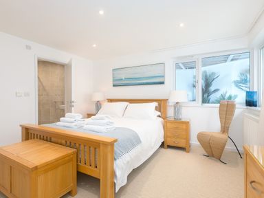 A bedroom with a wooden bed and nightstands with lamps towels on the bed and a door to a bathroom at Portside in Carbis Bay