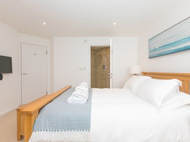 A bedroom with a wooden bed frame white bedding folded towels a lamp and a wall-mounted TV at Portside in Carbis Bay