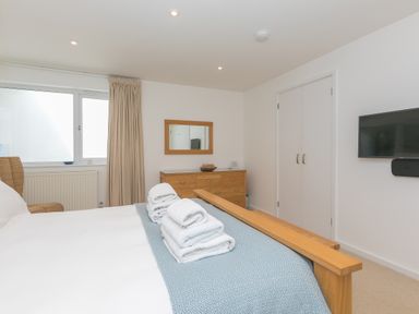 A bedroom with a wooden bed frame folded towels on the bed a wooden dresser with a mirror and a wall-mounted TV at Portside in Carbis Bay
