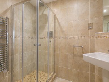 A bathroom with a glass shower enclosure a tiled floor and walls a towel rail and a sink at Portside in Carbis Bay