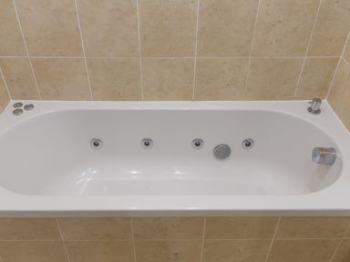 A white bathtub with jets and chrome fixtures set against beige tiled walls at Portside in Carbis Bay