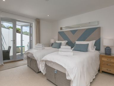 A bedroom with two single beds and folded towels on them with a bedside table and lamp near doors leading outside at Portside in Carbis Bay