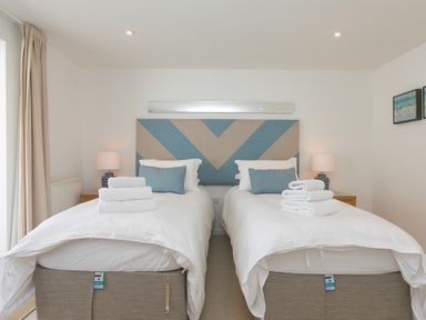 A bedroom with two single beds with blue and beige headboards and folded towels on top at Portside in Carbis Bay