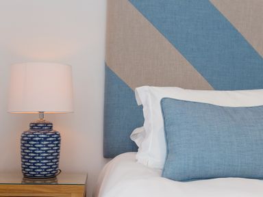 A bedside table with a blue patterned lamp and part of a bed with white sheets and a blue pillow at Portside in Carbis Bay