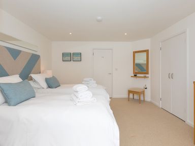 A bedroom with two beds with blue and beige headboards and towels on them a stool a mirror and a wardrobe at Portside in Carbis Bay